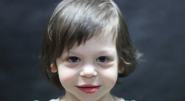 Portret dziecka z niebieskimi oczami i brązowymi włosami na ciemnym tle.