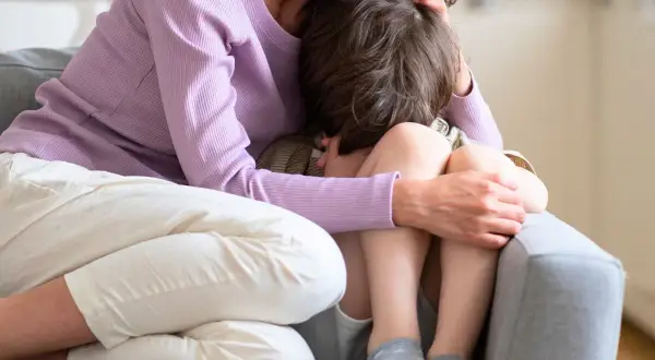 En mamma tröstar sitt barn som kramar sina knän. Barnet verkar oroligt, kanske upplever separationsångest.