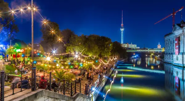 Serata vivace in un club all'aperto a Berlino, con luci colorate, gente che balla e la Torre della Televisione sullo sfondo.