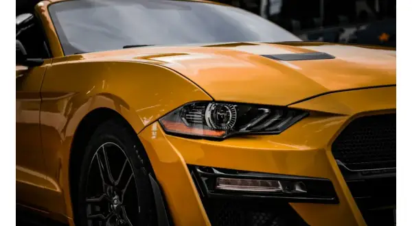Żółty Ford Mustang z błyszczącym lakierem, jakby był pomalowany farbą akrylową, z detalami reflektorów i grillem.