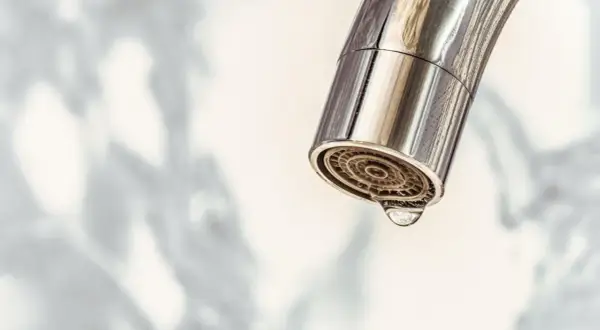 Nahaufnahme eines Chromwasserhahns mit einem Tropfen, der aus dem Sieb fällt. Zeit für das Wasserhahn Sieb reinigen.