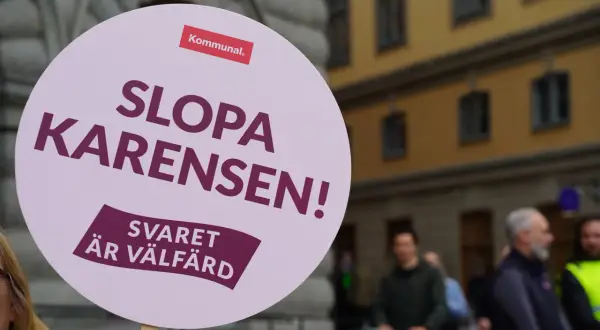En demonstration mot karensdag regler. Skylten lyder "Slopa karensen! Svaret är välfärd" och bär Kommunals logotyp.