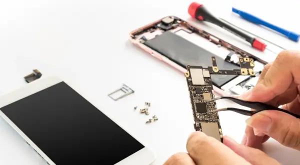 Naprawa telefonu: dłonie trzymające płytę główną, obok rozebrany smartfon i narzędzia.