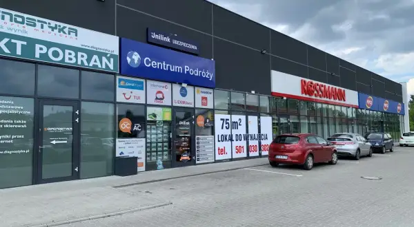 Budynek z szyldami "Diagnostyka", "Centrum Podróży", "Unilink Ubezpieczenia" i "Rossmann".