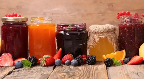 Słoiki z dżemami i miodem, otoczone świeżymi owocami. Pektyna co to? Naturalny zagęstnik do domowych przetworów.