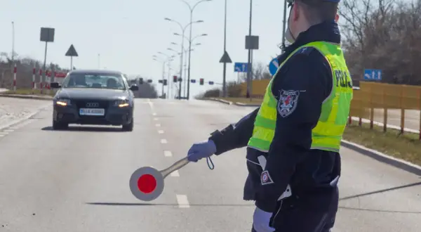Policjant kieruje ruchem, zatrzymując samochód. Może to być kontrola drogowa lub kurs reedukacyjny.