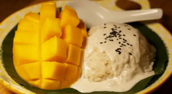 Ein Teller mit süßem Mango Sticky Rice, garniert mit Kokosmilch und Sesam. Ein köstlicher Nachtisch!