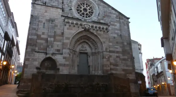 La iglesia de Santiago a Coruña, con su fachada de piedra y rosetón, se alza imponente en una calle adoquinada.