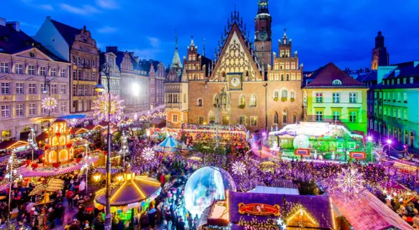 Tłoczny jarmark we Wrocławiu nocą, rozświetlony tysiącami lampek. Widać Ratusz, karuzelę i stragany.