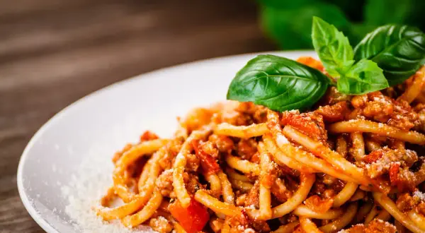 Talerz spaghetti z sosem bolońskim, posypany parmezanem i udekorowany bazylią.
