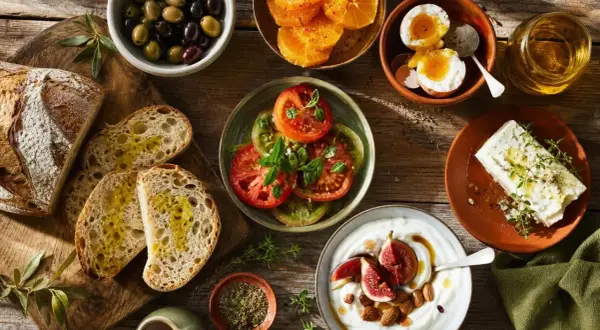 Un petit-déjeuner méditerranéen avec pain, olives, tomates, œufs, fromage, yaourt et fruits. Parfait pour savoir que cuisiner cette semaine.