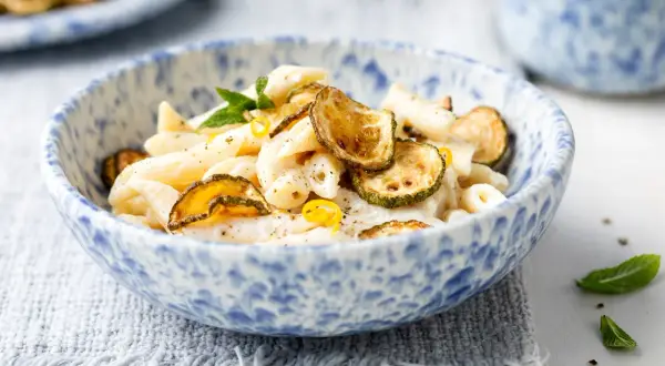 Piatto di pasta cremosa con ricotta e zucchine croccanti, guarnito con scorza di limone e menta.