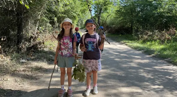 Dwie dziewczynki z patykami w rękach na leśnej ścieżce. Bory Tucholskie oferują wiele atrakcji dla dzieci, jak ta leśna wyprawa.