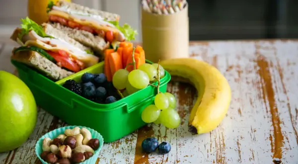 Gesunde Lunchbox mit Sandwiches, Beeren, Trauben, Karotten, Nüssen und Obst. Perfekt für kalorienarme Snacks unterwegs.