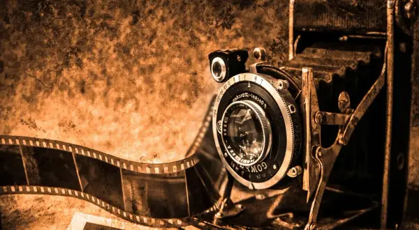 Antyczna kamera i rolka kliszy, świadkowie pierwszych fotografii, w sepia tonacji.