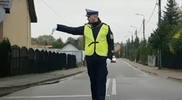 Policjant w kamizelce odblaskowej kieruje ruchem na ulicy, wskazując ręką kierunek.
