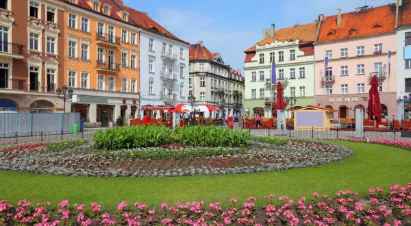 Kolorowy rynek w najstarszym mieście w Polsce, z kwitnącymi rabatami kwiatowymi i kolorowymi kamienicami w tle.