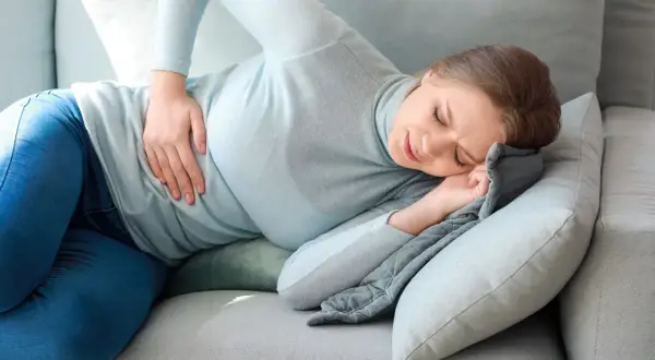 Kobieta z bólem brzucha szuka ulgi, wypróbowując na ból brzucha domowe sposoby.
