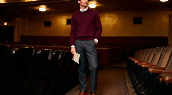 Uomo elegante in maglione bordeaux e pantaloni grigi, pronto per andare a teatro. Un esempio di come vestirsi per andare a teatro con stile.