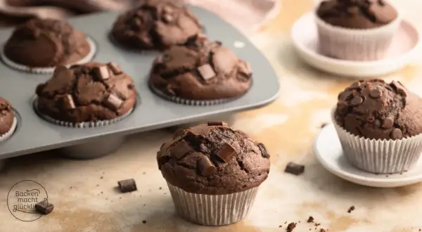 Schokomuffins mit Schokostückchen, perfekt für Kinder. Ein Muffin liegt vorne, weitere im Blech und auf Tellern.