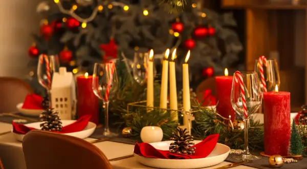 Uroczysta wigilia w restauracji: pięknie nakryty stół z czerwonymi świecami, szyszkami i choinką w tle.