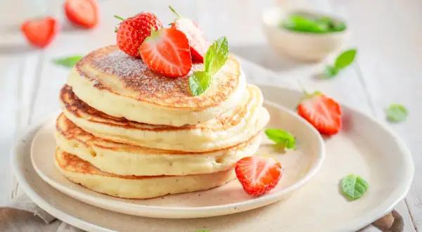 Pancake con yogurt e fragole fresche, spolverati di zucchero a velo e decorati con foglie di menta.