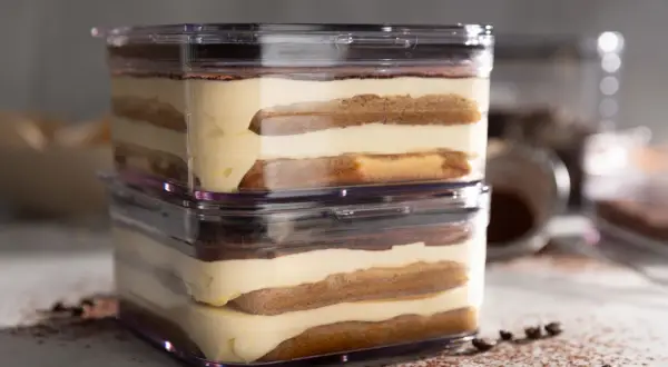 Zwei Schichten sally tiramisu im transparenten Behälter, mit Kakaopulver und Kaffeebohnen bestreut.