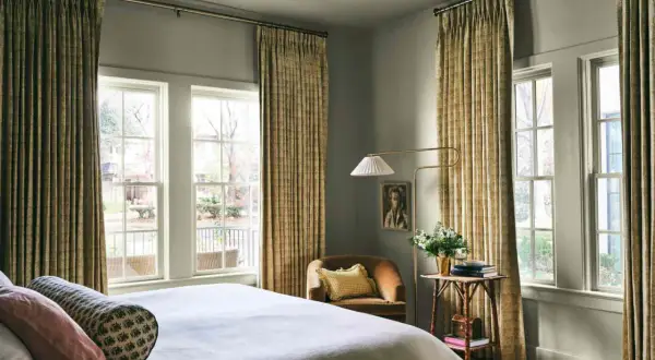 A cozy bedroom with a bed, a chair, and a floor lamp. The curtains are a beautiful millenial green, adding a touch of nature to the room.