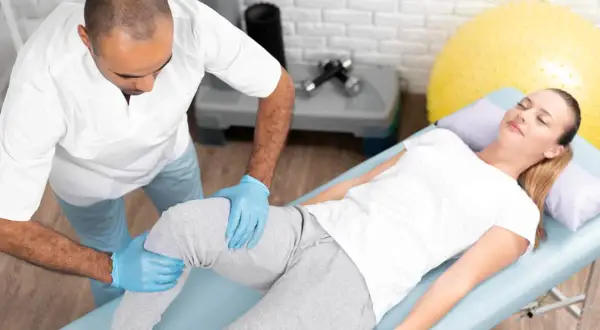 Fizjoterapeuta wykonuje masaż podczas rehabilitacji po operacji kolana. Kobieta leży na kozetce, zrelaksowana.