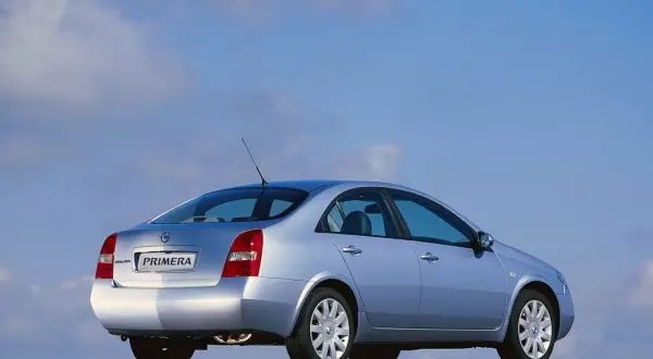 Srebrny Nissan Primera 2002 z widokiem z tyłu, zaparkowany na drodze pod błękitnym niebem.