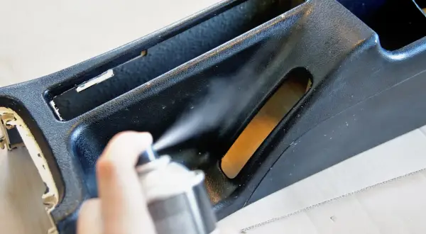 Ręka trzyma puszkę z farbą w sprayu, odświeżając czarne plastiki w aucie.