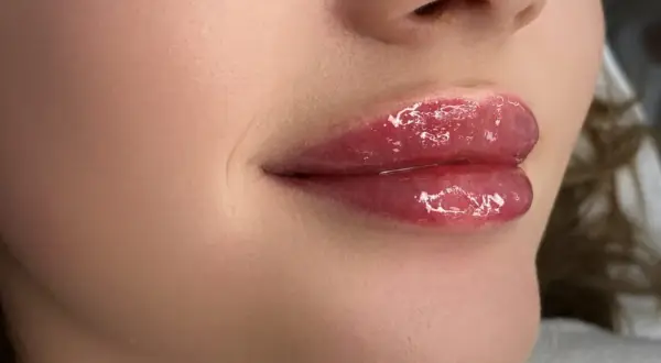 Błyszczące, pełne usta z delikatnym połyskiem, przypominające baby doll lips.