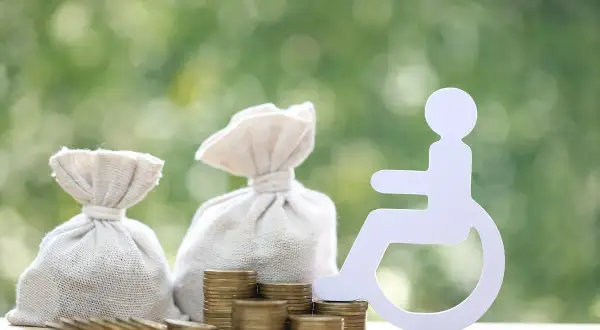 Symbol osoby na wózku inwalidzkim obok worków z pieniędzmi i monet sugeruje świadczenie wspierające kwoty.