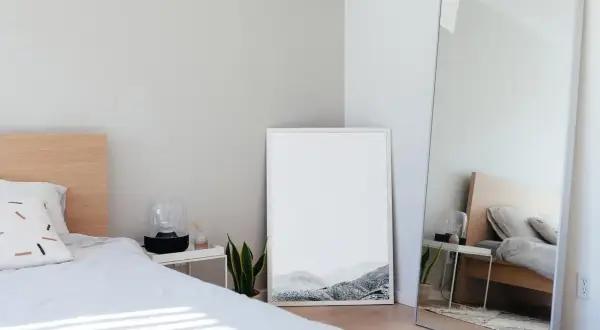 Jasne, minimalistyczne lustro w sypialni feng shui odbija łóżko i tworzy wrażenie większej przestrzeni.