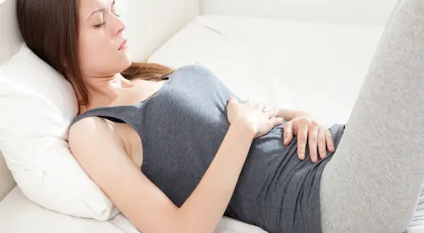 Donna sdraiata su un fianco, con le ginocchia piegate e le mani sull'addome, in una **posizione antalgica** per alleviare il dolore.