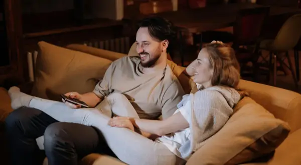 Ett par myser i soffan, skrattar och tittar på TV. Deras närhet och gemensamma skratt är grundstenar i en relation.