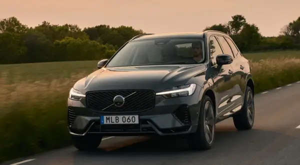 Ciemnoszary Volvo XC60 2025 jedzie drogą wśród zieleni o zachodzie słońca.