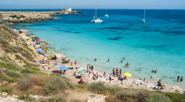 Spiaggia di Favignana, dove si trova questo paradiso azzurro con gente che si gode il sole e il mare cristallino, con barche all'orizzonte.