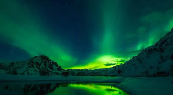 Reykjavik zorza polarna kiedy? Zielone światła tańczą nad ośnieżonymi górami i spokojną wodą.