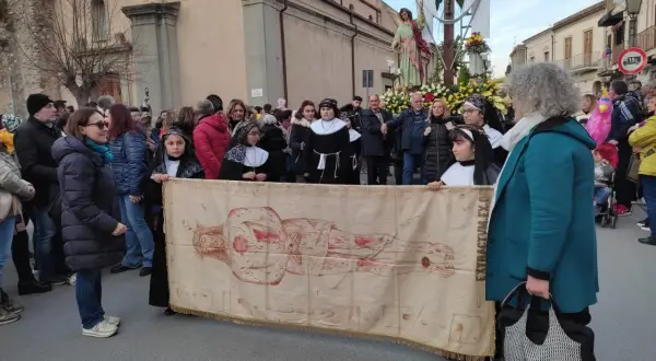 Processione con il telo della Veronica, raffigurante Cristo, tra la folla e una statua lignea.