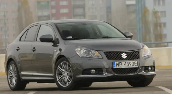 Szary Suzuki Kizashi z felgami i tablicą rejestracyjną WB 4890E na tle budynków.