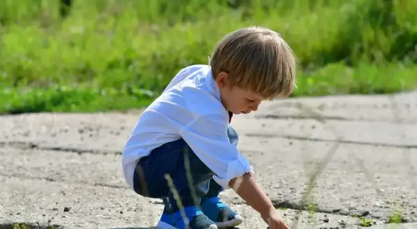 Mały chłopiec w białej koszuli i jeansach pochyla się nad ziemią, jakby szukał czegoś. To scena z mojego dzieciństwa, jak z tekstu piosenki "kiedy byłem małym chłopcem".