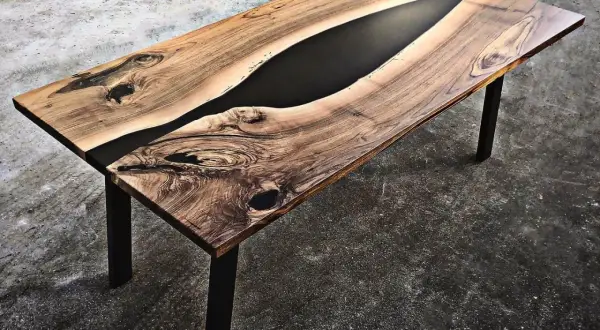 Tavolo in legno con venature naturali e un inserto centrale di resina per tavoli nera, che crea un contrasto moderno e affascinante.