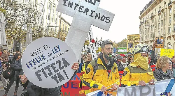Manifestantes protestan contra el fraude de ley y el abuso de temporalidad, exigiendo fijeza. Un cartel en forma de cruz dice "RIP INTERINOS", reflejando el deseo de no ser interino toda la vida.