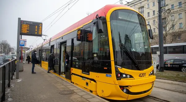 Nowy, żółto-czerwony 17 tramwaj warszawa z numerem 4201 stoi na przystanku. Pasażerowie wsiadają.