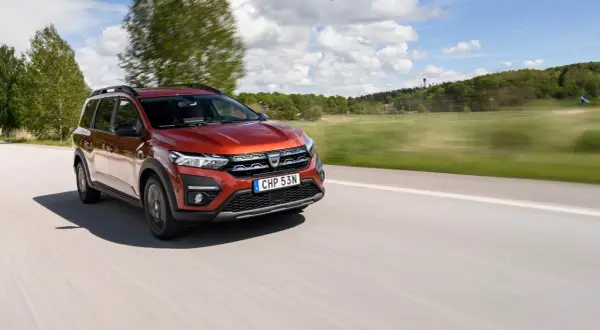 En röd Dacia Jogger begagnad kör på en landsväg i Sverige. Bilen är i rörelse med suddig bakgrund.