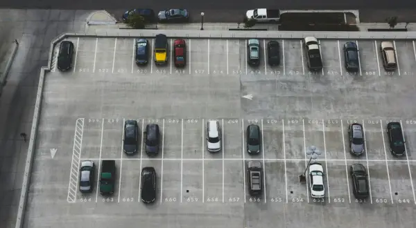 Widok z góry na parking. Samochód cofający na parkingu, kto ma pierwszeństwo? Wiele zaparkowanych aut.