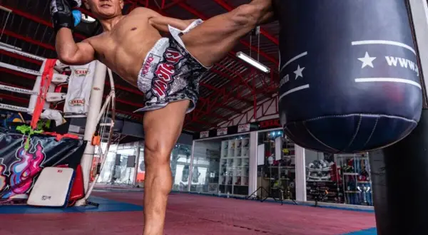 A Muay Thai fighter delivers a powerful kick during pad work boxing training in a gym.