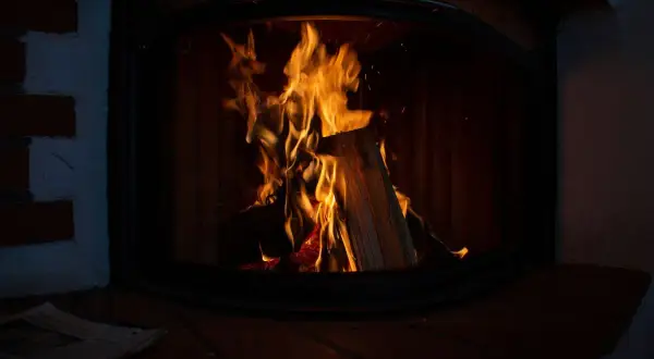 Flammen lodern im Kaminofen. Ein Zeitungsstapel liegt davor. Der Ofen ist nicht stillgelegt, es gibt Ausnahmen für gemütliche Abende.