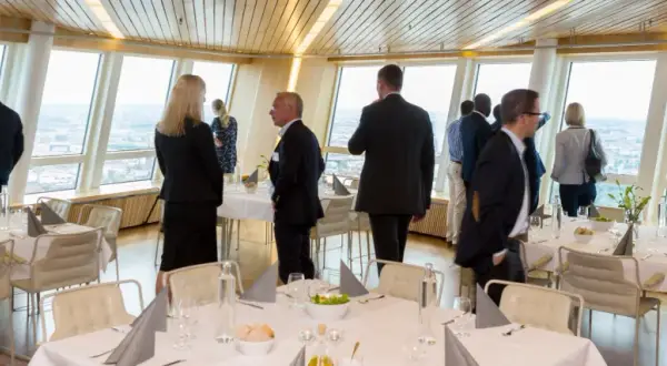 Människor i affärs kläder njuter av utsikten från en restaurang. En turning torso visning av staden.